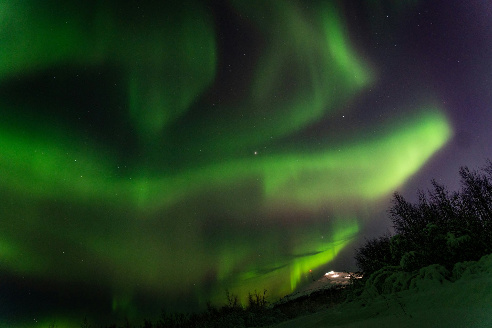 Green aurora borealis over a snowy Kiruna landscape at night